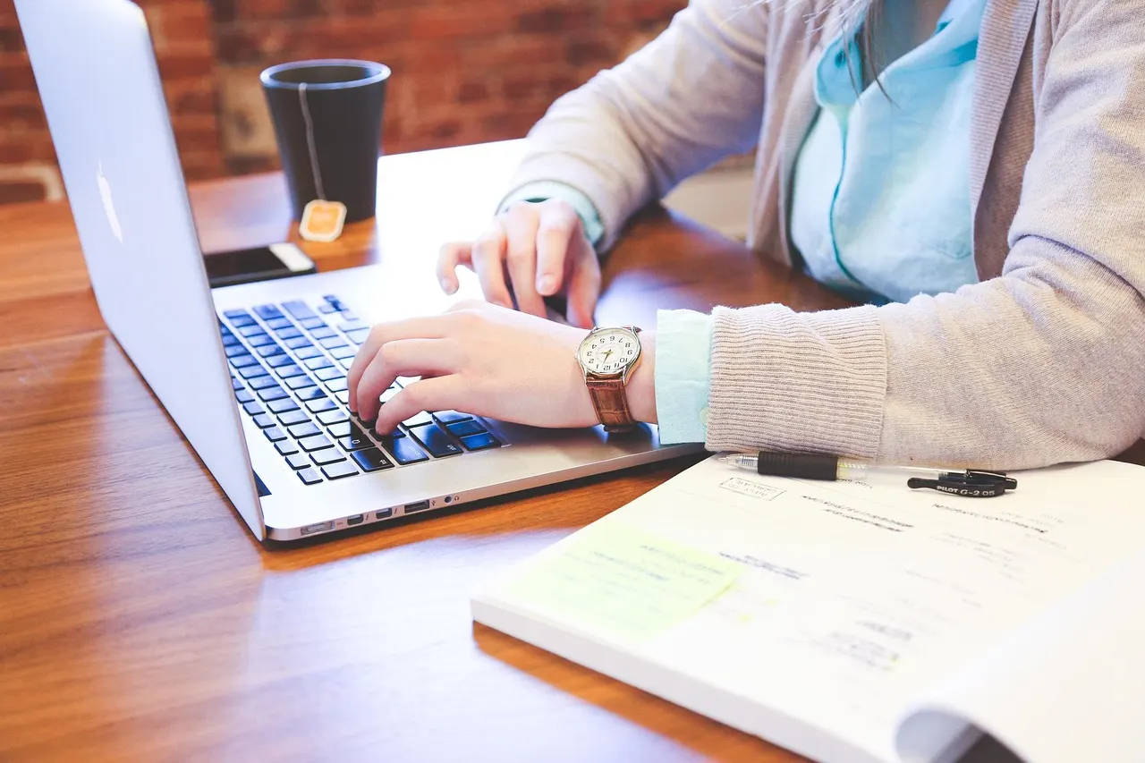 Hands typing on a laptop at a wooden desk while planning an email newsletter